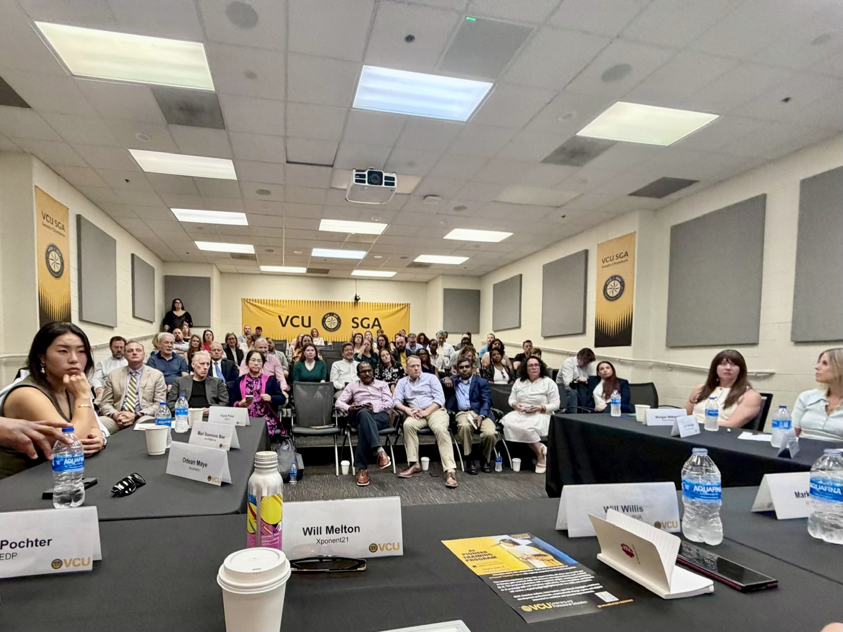 Audience members seated in the VCU Senate Chambers raise their hands and ask questions during the roundtable.