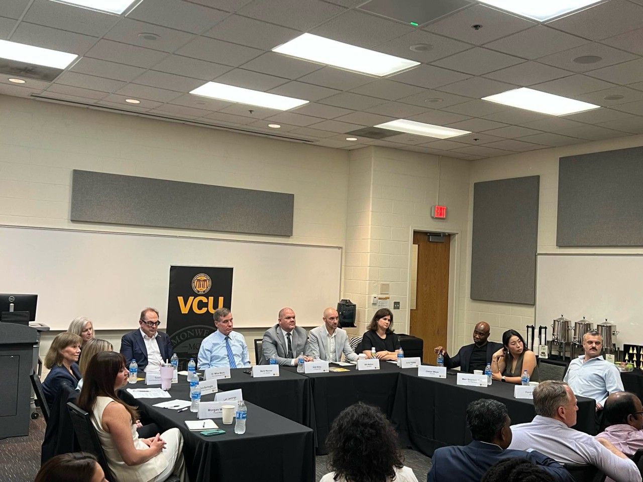 Roundtable participants seated at a table with name cards discuss AI workforce policy with Sen. Mark Warner.